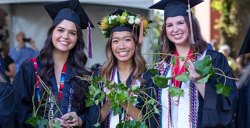 Three female students in their caps and gowns proudly hold their ivy at SPU's Ivy Cutting ceremony